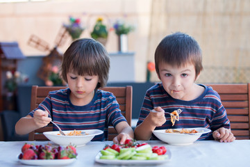 Cute children, preschool boys, eating spaghetti for lunch outdoors in garden