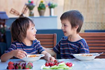 Cute children, preschool boys, eating spaghetti for lunch outdoors in garden