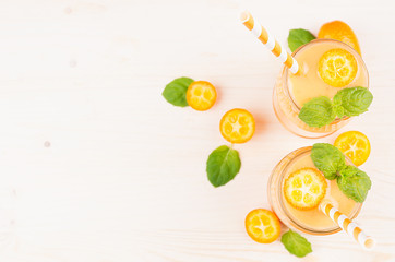 Orange citrus kumquat  fruit smoothie in glass jars with straw, mint leaf, cute ripe berry, top view. White wooden board background, copy space.