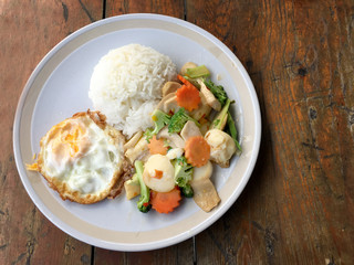 mixed fried vegetable tofu with rice and fried egg in white dish on wooden background. Vegetarian Food, healthy food.