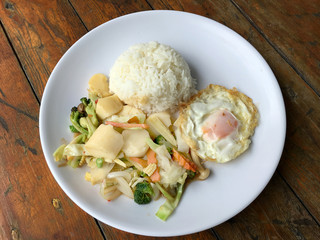 Stir-fried mixed vegetables with tofu and fried egg with rice in white dish on wooden background.  Vegetarian Food, healthy food.