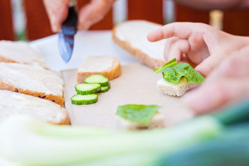 Gradfather and grandson eating bread with cream cheese together. Close-up photo of their hands, boy holding a piece of bread with cream cheese and fresh spinach leaf. 