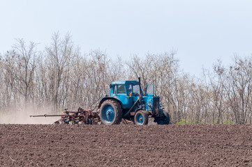 An old tractor in the field plows the land. Spring landscape of a countryside, a farm.