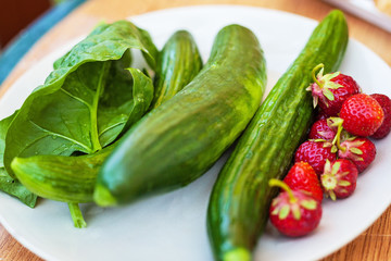 Plate of fresh cucumber, spinach and strawberries, view from above, placed on a old outdoor table