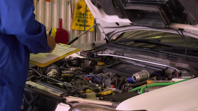 Auto mechanic calculates the cost of repairs on the background of the open hood close-up.