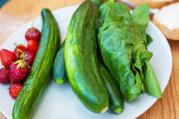 Plate of fresh cucumber, spinach and strawberries, view from above, placed on a old outdoor table