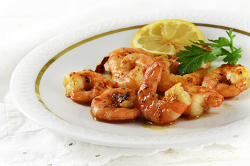 fried tiger prawns, marinated with garlic, spices, herbs and lemon on a fine white plate, italian parsley garnish, bright background