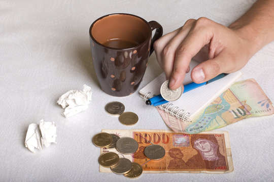 Macedonian money, cup of coffee, piece of paper and pen, and man's hand holding 50 denars coin