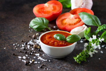 Tomato ketchup sauce in a bowl with spices, basil leaves and tomatoes on the kitchen table.