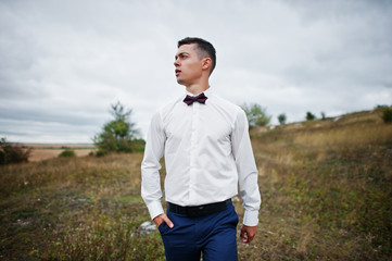 Naklejka na ściany i meble Handsome groom in the middle of the meadow surrounded by tall grass, bushes and rocks.