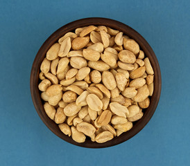 Roasted salted peanuts in bowl  on blue background, top view