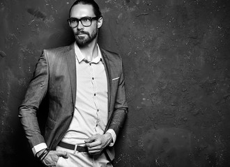 portrait of handsome fashion stylish hipster businessman model dressed in elegant brown suit in glasses posing near dark wall in studio