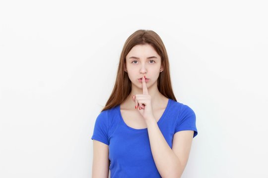Portrait of young woman keeping finger on her lips and asking to keep quiet, isolated over white background