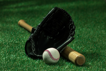 Closeup view of baseball bat, glove and ball lying on green grass