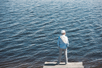 Fototapeta na wymiar back view of casual man standing on quay in front of water surface at daytime