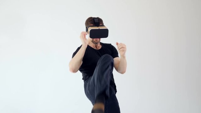 A man wearing virtual reality headset and making moves as if fighting with someone. White background. 4K.