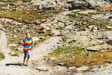 Obraz premium Cute little girl wearing bright rainbow colored coat and beige boots, resting in mountains, Switzerland