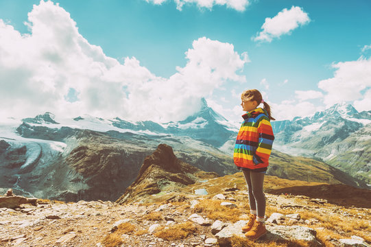 Cute little girl wearing bright rainbow colored coat and beige boots, resting in mountains, Switzerland, vintage image