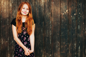 Obraz premium Outdoor fashion portrait of happy red-haired girl, posing against old wooden background