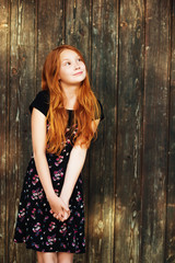 Fototapeta premium Outdoor fashion portrait of happy red-haired girl, posing against old wooden background