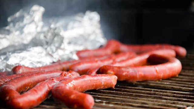 Seamless loop - Tasty juicy sausages grilling  on a barbecue with potatoes in foil, barbecue concept, video HD