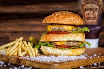 Delicious Homemade Maxi Burger with grilled beef steak, lettuce, cheese, tomato, onion, barbecue sauce, honey mustard, fries, pickles