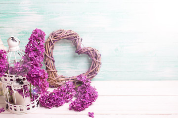 Violet lilac flowers, decorative heart and lantern on white wooden background against turquoise wall.