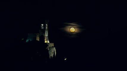 timelapse of night view of rising full moon near medieval clock tower in the almost complete dark in Italy