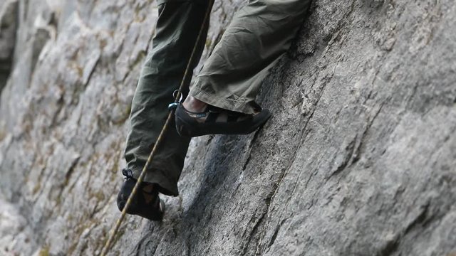 Detail of strong healthy young rock climbing man, legs and feet. Climber steps left and then up. Security harness, rope and quickdraw. Slow motion at 120 fps. Patagonia Argentina.