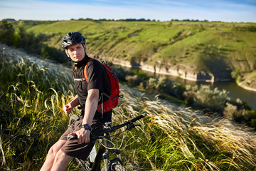 Attractive cyclist standing with mountain bike against beautiful landscape.