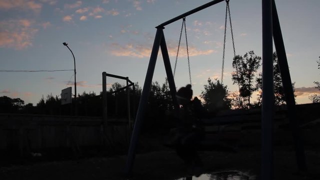 sad child swinging on a swing on a dark sky background. child abuse, painful childhood