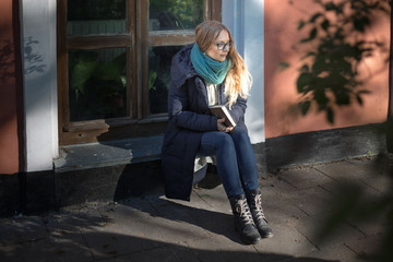 The girl is reading a book sitting by the window