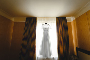 luxury wedding dress hanging on window in a hotel room