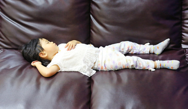 baby child girl age about one years eight month sleeping on brown leather sofa.