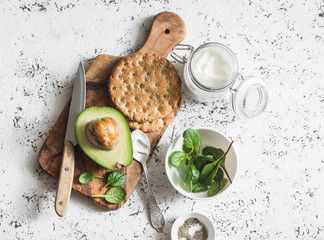 Healthy breakfast or snack - avocado, Greek yogurt and crackers on a light background, top view....
