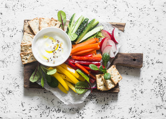 Healthy snack - raw vegetables and yogurt sauce on a wooden cutting board, on a light background,...