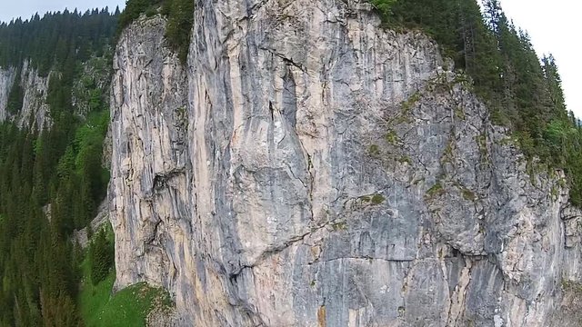 Flying towards spectacular tall rock limestone wall covered with fir trees , alpine landscape in Zanoaga Gorge, Bucegi Natural Park , Romania, aerial view