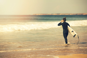 young surfer girl wearing wetsuit going into the ocean to surf at sunset