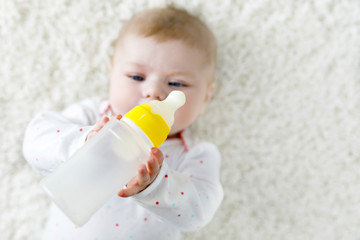 Cute adorable ewborn baby girl holding nursing bottle and drinking formula milk