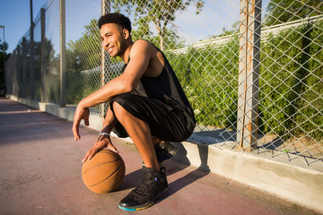 Basketball player is sitting on a basketball court.street ball,sport competitions,afro,outdoor portrait,sport games,handsome black man,pretty,man holding ball,sportsman,black sport shorts,sports shoes