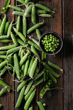 Young organic green pea pods and peas in bowls over old dark wooden planks background. Top view with space. Harvest, healthy eating.