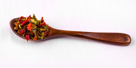 Hot spices in a wooden spoon on a white wooden table.