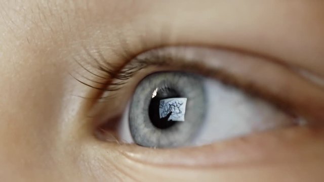 Closeup of blue eye of little boy looking at digital tablet while drawing something on screen