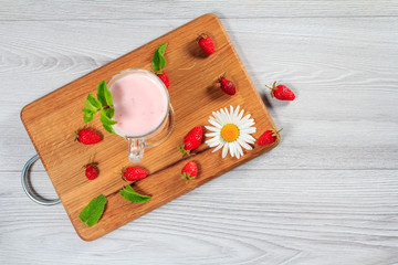 Glass of milk shake with mint and fresh strawberries on a wood cutting board