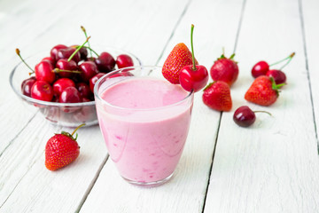 Milkshake made of mix - cherry and strawberry and tasty berries on white wooden table.