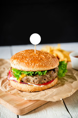 Classic big hamburger with beef, sauce and french fries on dark background. American tasty food. White frame