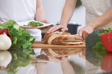 Close-up of human hands slicing bread in a kitchen. Friends having fun while preparing fresh salad. Chef cook represent culinary masterclass. Vegetarian, healthy meal and friendship concept