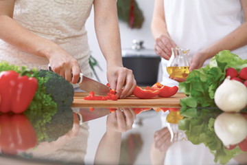 Close-up of four human hands are cooking in a kitchen. Friends having fun while preparing fresh salad. Vegetarian, healthy meal and friendship concept
