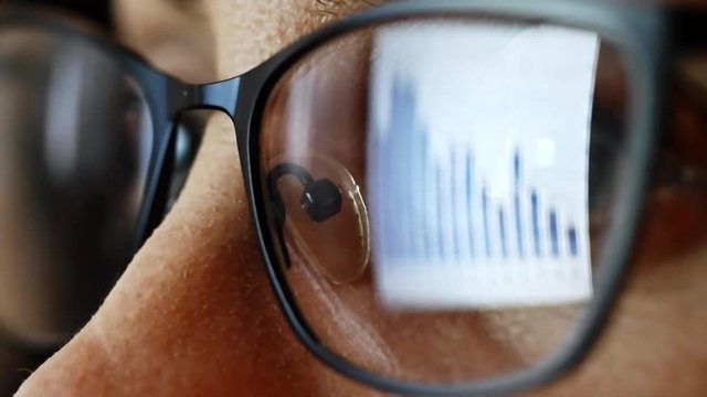Closeup of eyes of businesswoman in glasses looking at computer screen with financial bar graph on it