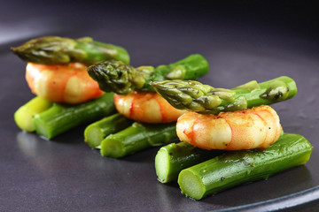 green asparagus with a tiger prawn, festive appetizer or buffet snack on a gray plate, close up